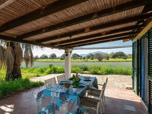Un espacio de comedor al aire libre con una mesa lista para dos, con vistas a un lago y follaje.