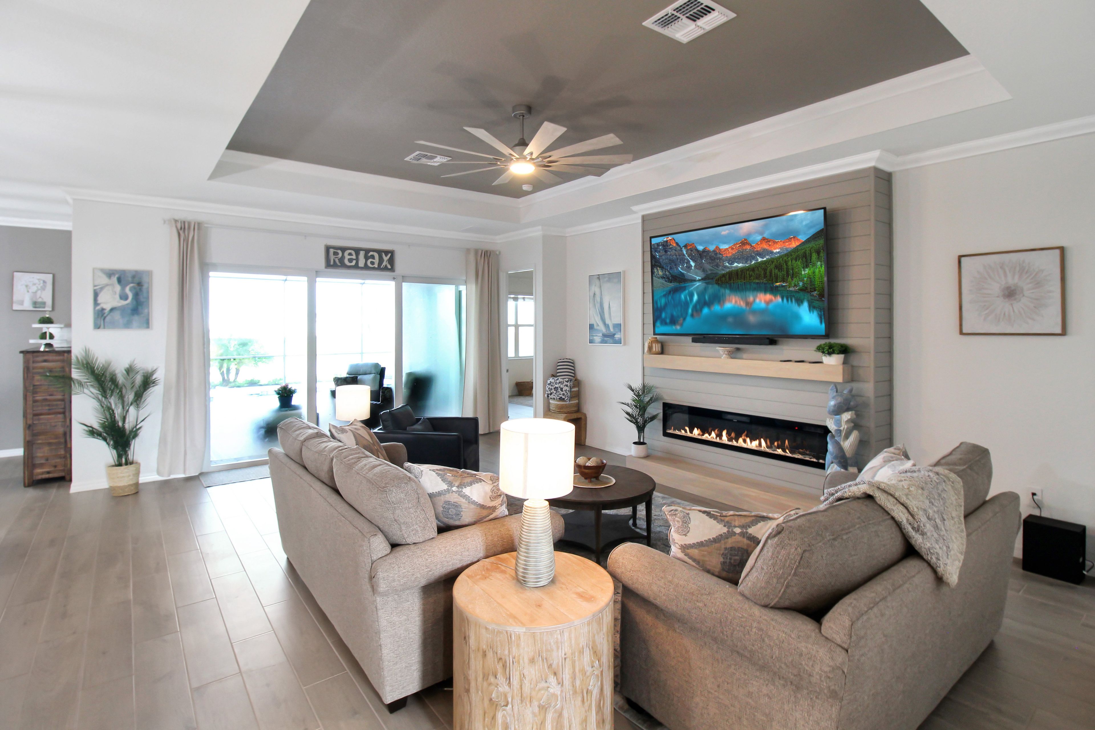 A modern living room with a fireplace, a large flat-screen TV, and a ceiling fan.