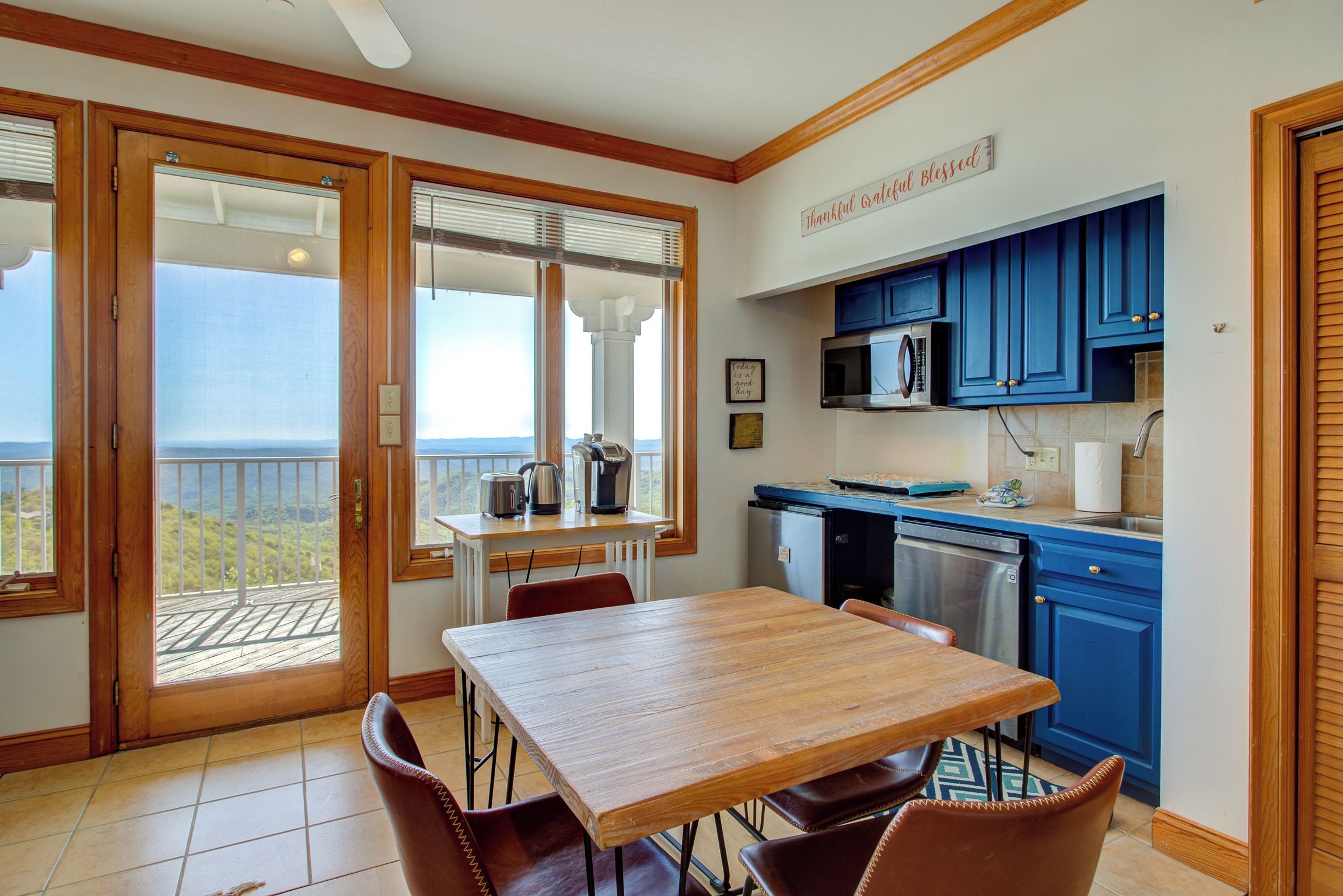 A kitchen with a view of the mountains, a dining area with a table and chairs, and a sign that says 'Thankful Grateful Blessed'.
