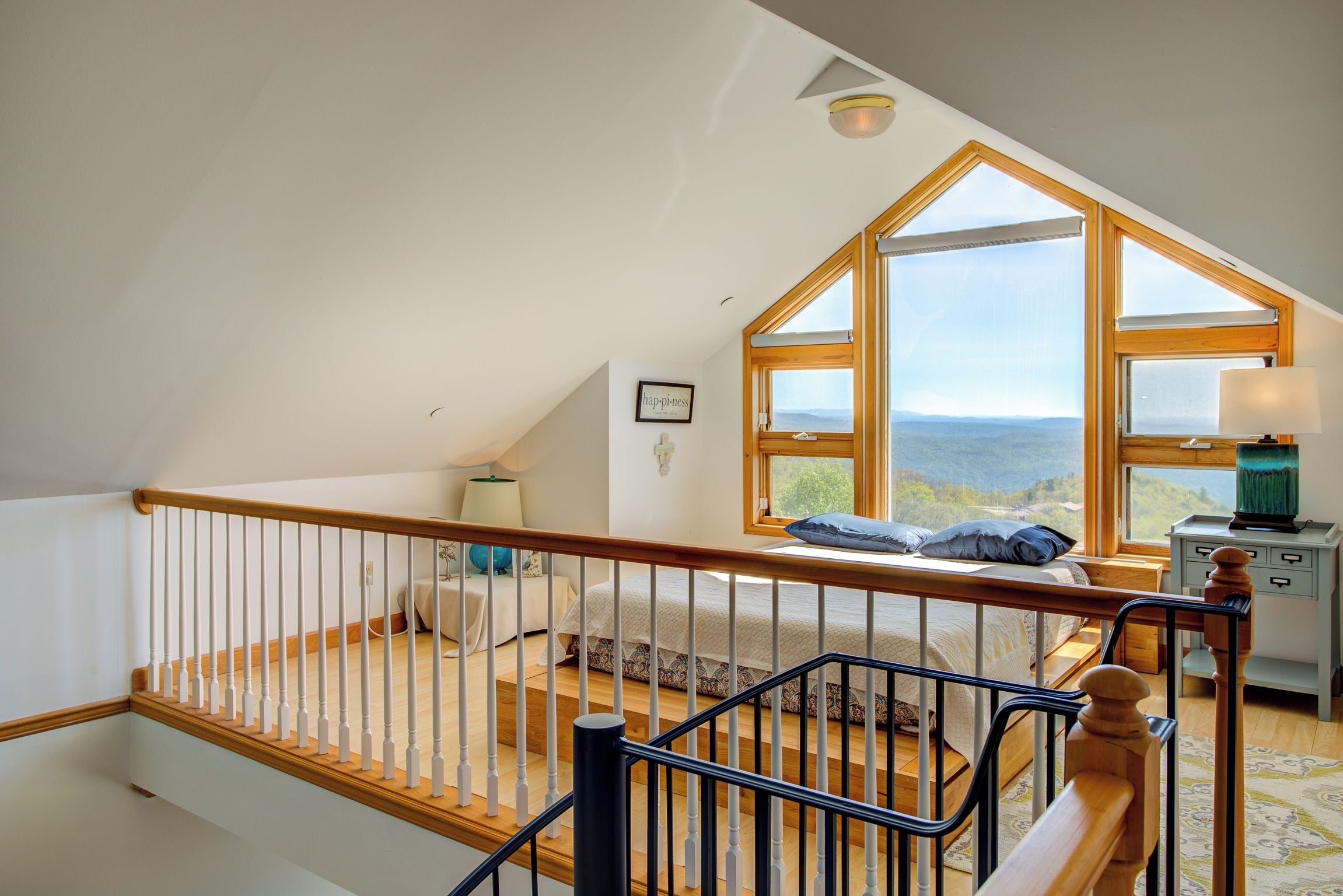 A bedroom with a sloped ceiling, a bed, a desk, and a view of the landscape.
