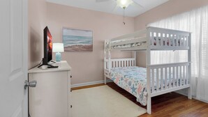 Een kinderkamer met stapelbedden, een bureau met computer en lamp, en een plafondventilator.