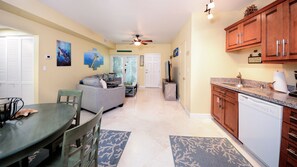 A spacious living area with a sofa, a dining table, and a kitchen area with wooden cabinets and a dishwasher. - 811 Mariner's Club | Luxury Resort affordably priced (Key Largo)