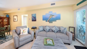 A living room with a grey sofa, a coffee table, and a dining area with a wooden table and chairs. - 811 Mariner's Club | Luxury Resort affordably priced (Key Largo)