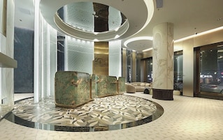 Un moderno vestíbulo de hotel con una zona de estar circular, un mostrador de recepción y un pilar grande.