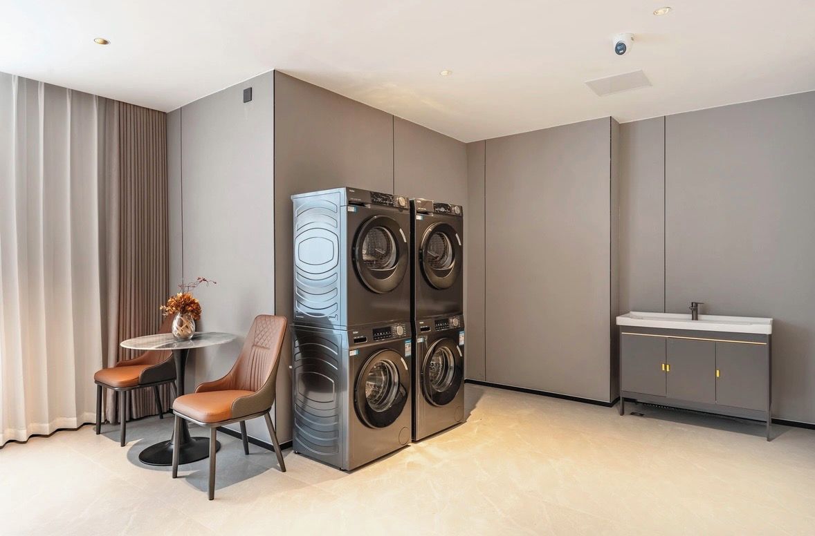 A compact, modern laundry room with a built-in washer and dryer, a small round table with chairs, and a minimalist sink area.