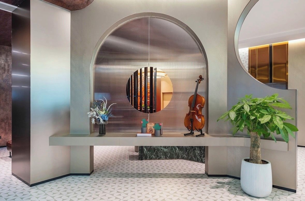 Un área de recepción de diseño moderno, con una pared curva, una vitrina de vidrio con un violín y una planta en maceta.