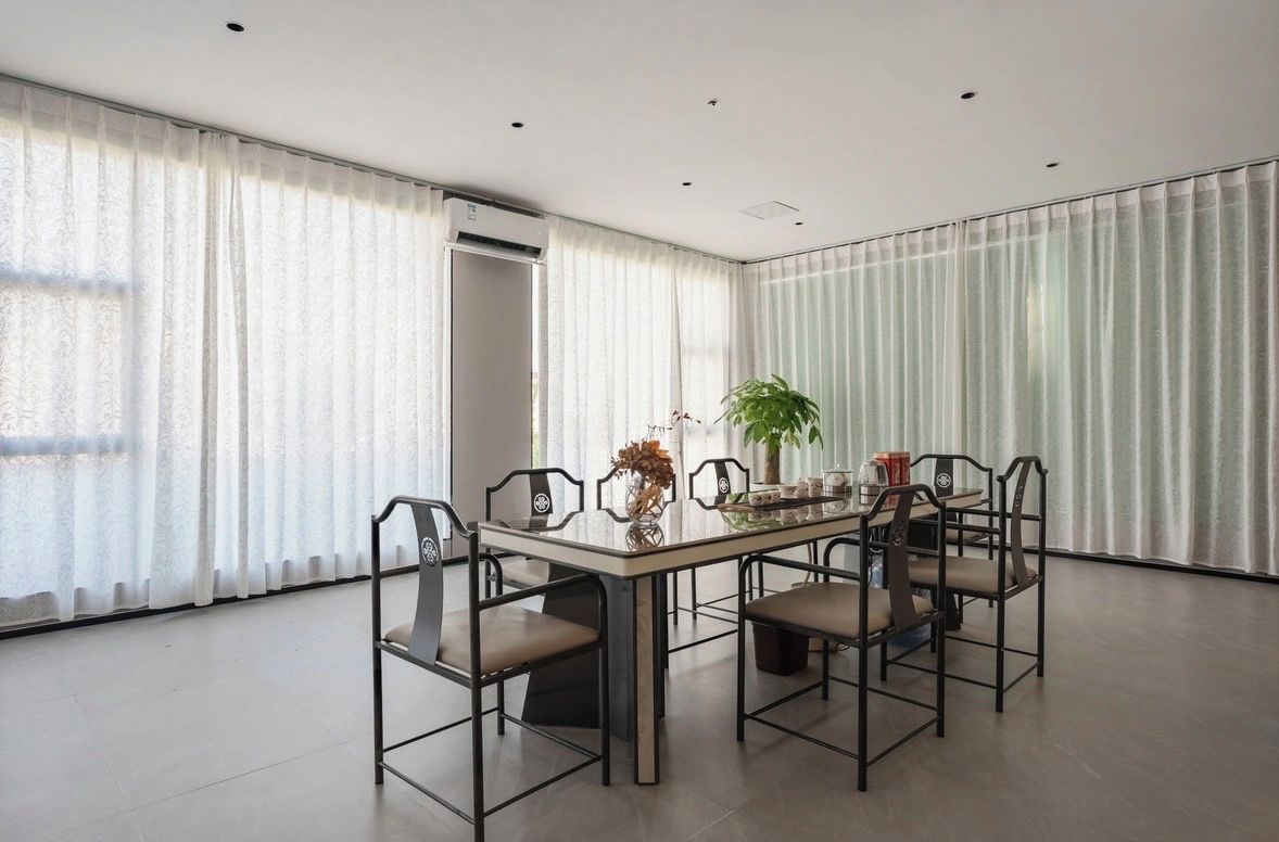 A dining area with a table and chairs, a potted plant, and a window with curtains.