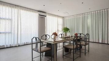 A dining area with a table and chairs, a potted plant, and a window with curtains.
