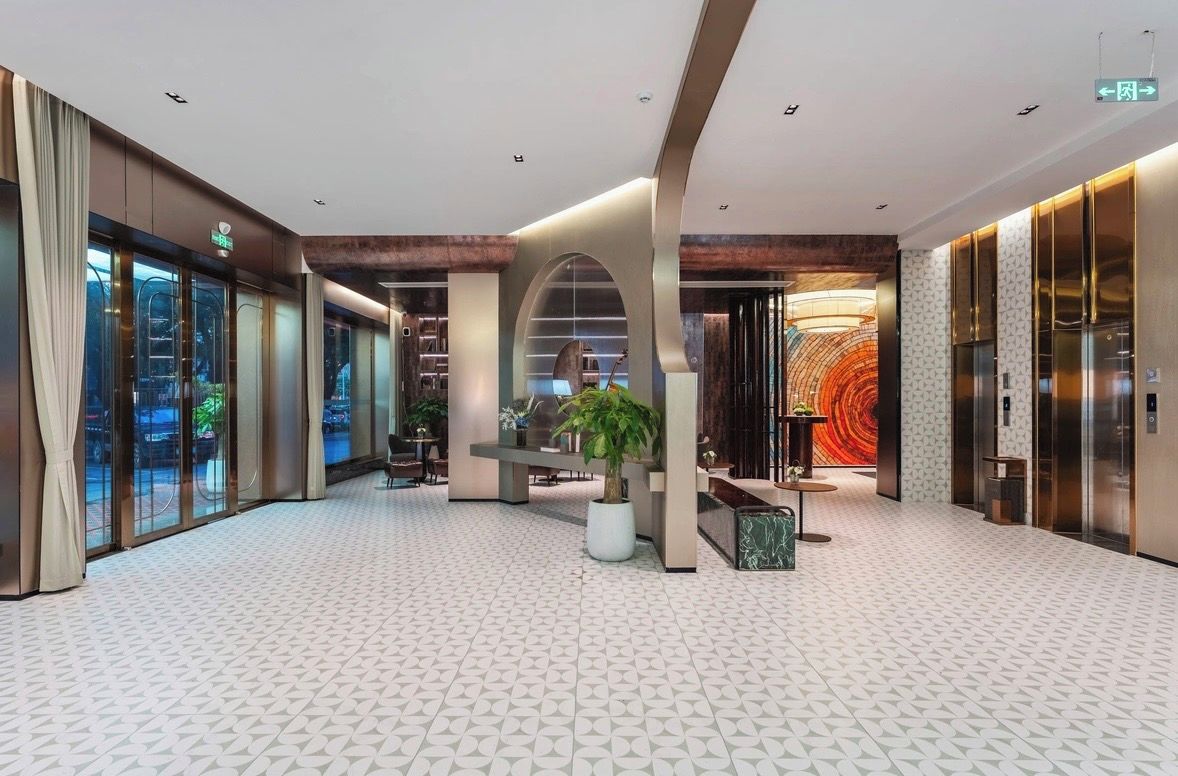 A modern hotel lobby with a geometric patterned floor, a central seating area, and a large wall mural.