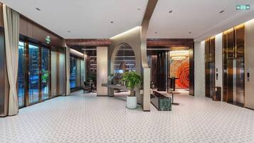 A modern hotel lobby with a geometric patterned floor, a central seating area, and a large wall mural.