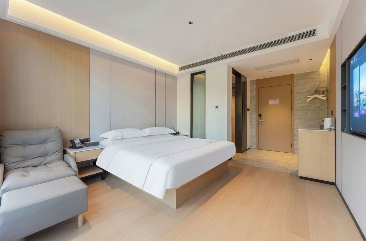 A modern hotel room with a bed, a sofa, a desk with a telephone, and a television.