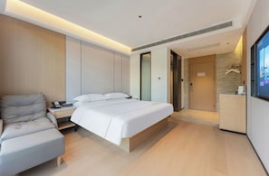 Ein modernes Hotelzimmer mit einem Bett, einer Couch, einem Schreibtisch mit Telefon und einem Fernseher.