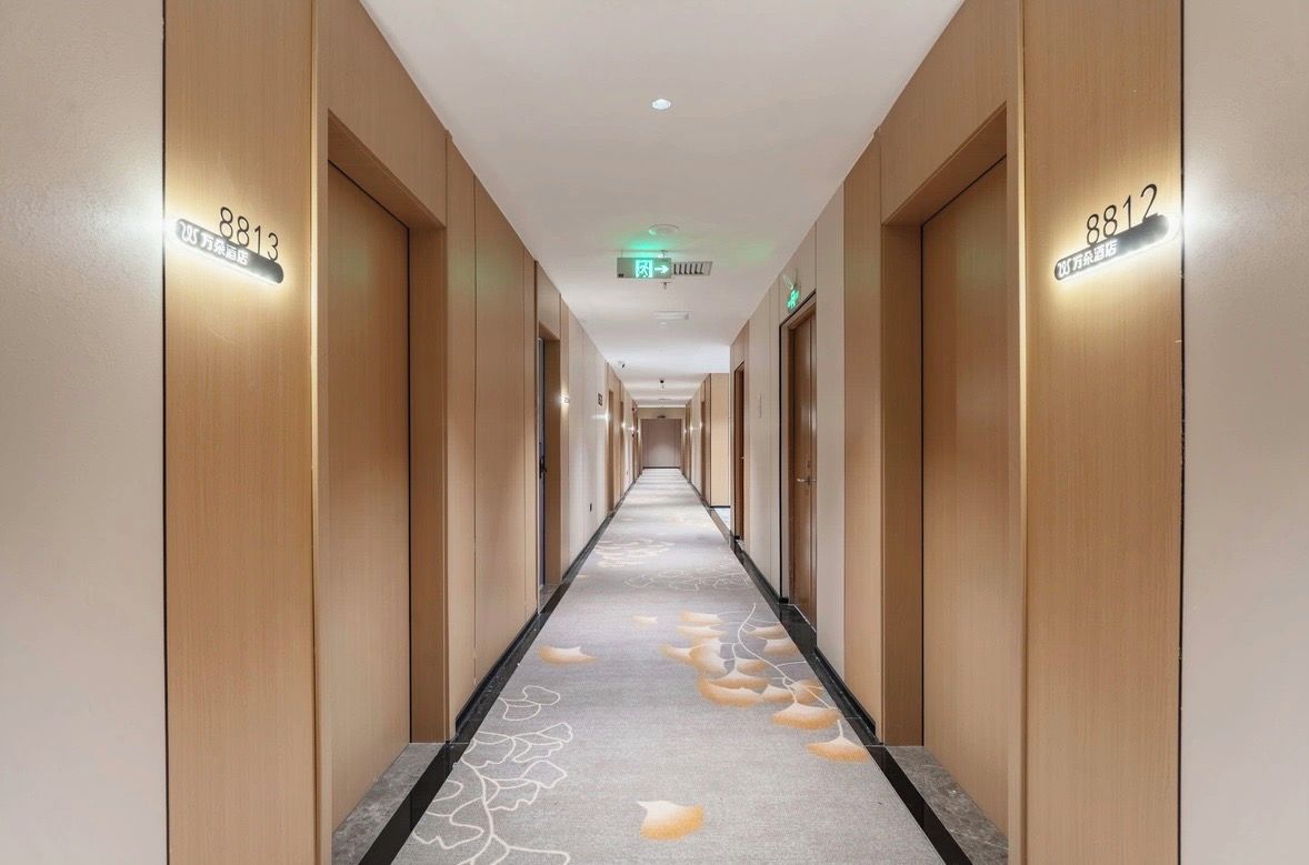 Corredor de hotel com portas de madeira, numeradas 8813 e 8812, e um tapete com padrão de folhas.