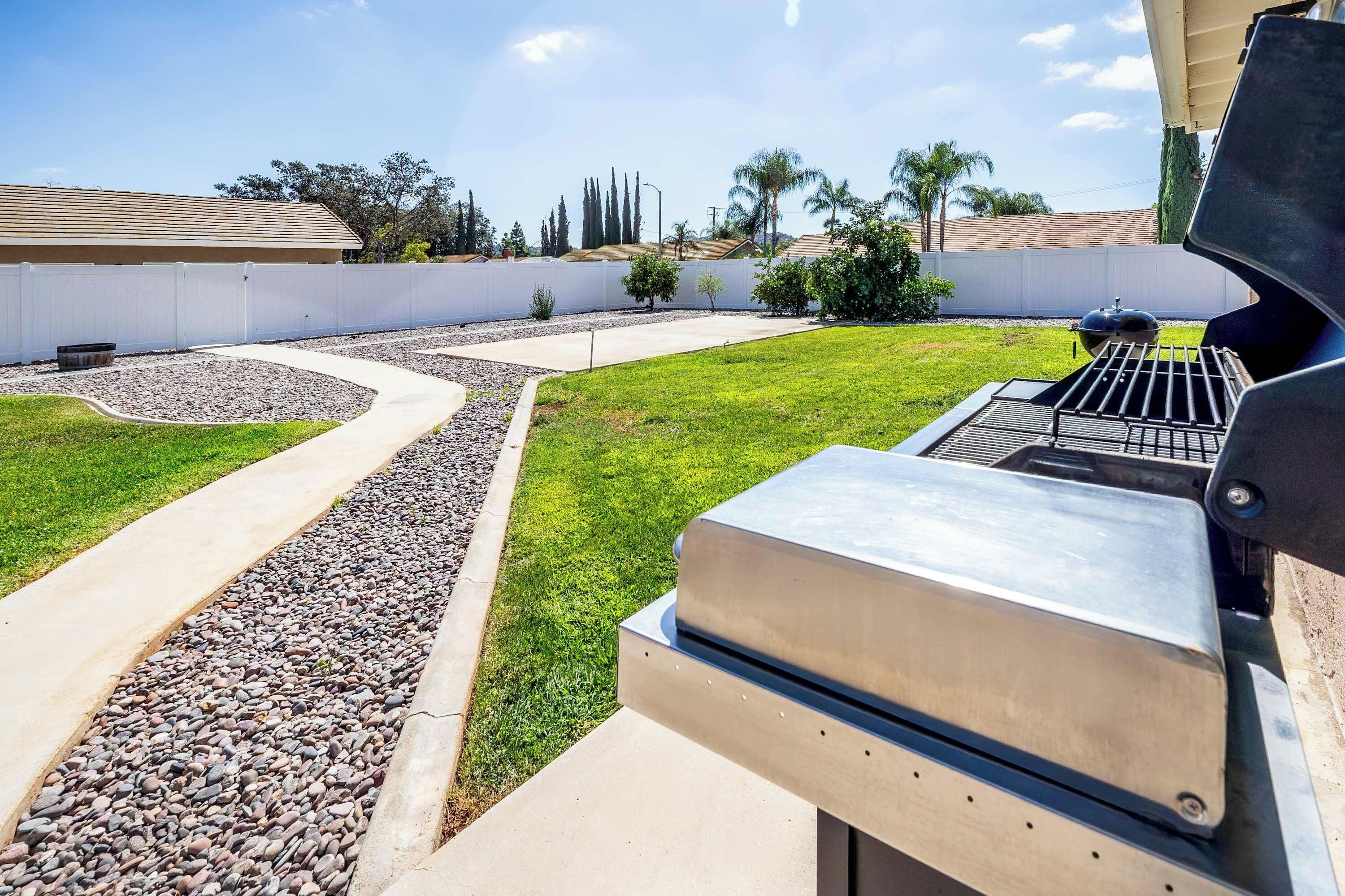 Un jardin avec un barbecue, un chemin sinueux et une pelouse.