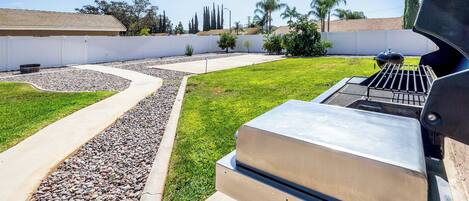Un jardin avec un barbecue, un chemin sinueux et une pelouse.