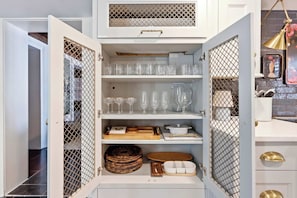 A storage cabinet with multiple shelves containing glassware, wooden bowls, and woven baskets. - Brick & Beam | Luxury Garden Apartment | 1855 (Savannah)