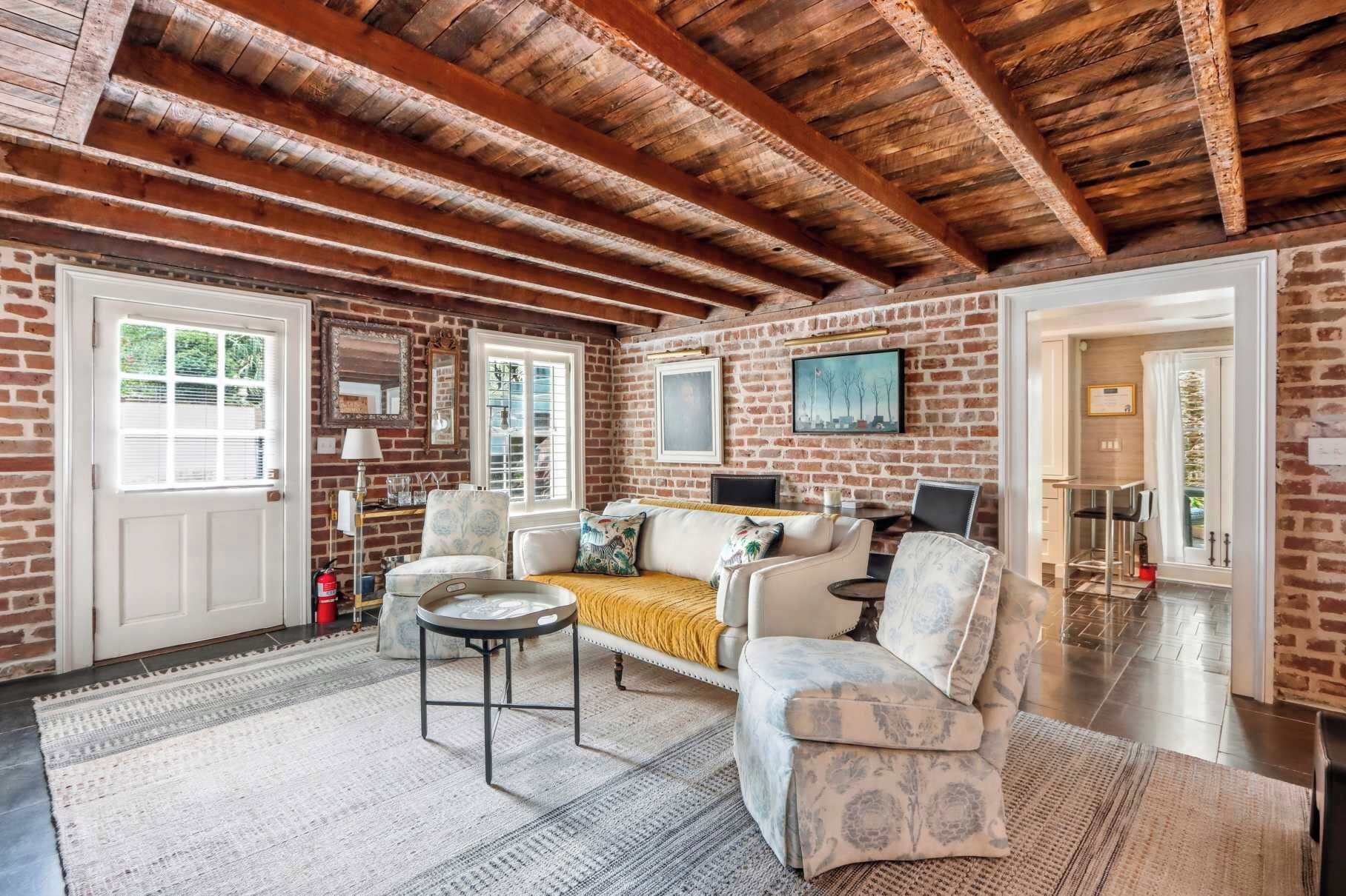 A cozy room with exposed wooden beams, a brick wall, a sofa, a coffee table, and a painting.