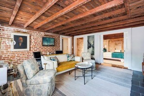 Ein Zimmer mit Backsteinwand, einer Couch, einem Couchtisch und einem Bett, das durch eine offene Tür zu sehen ist.