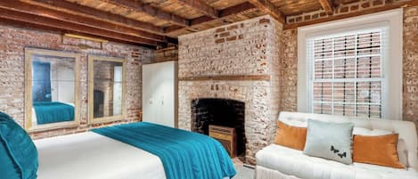 A room with a bed, a sofa, a fireplace, and a brick wall.