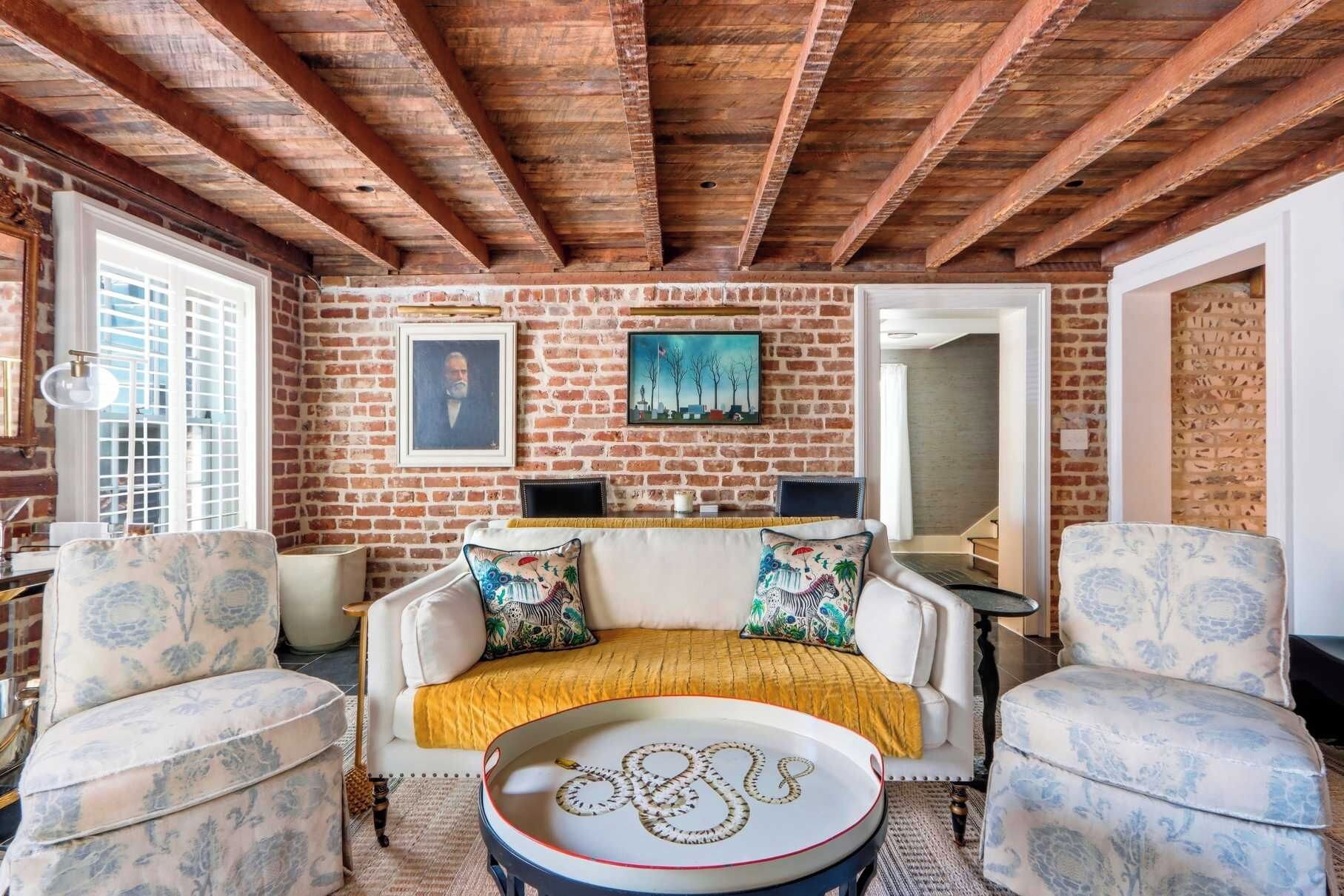 A cozy room with exposed wooden beams, a brick wall, and a sofa with patterned cushions.
