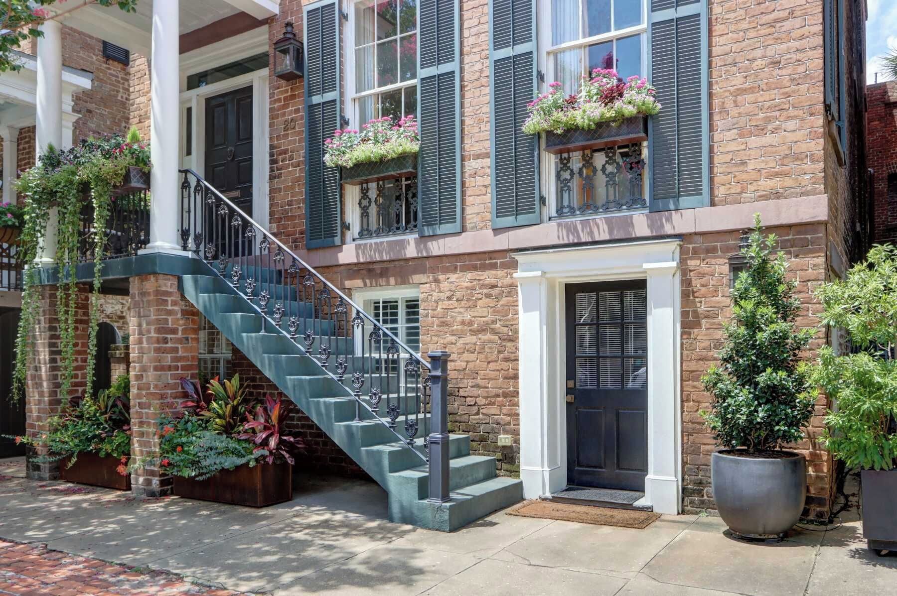 Un bâtiment à deux étages, construit en briques, avec un escalier, une porte d’entrée et des plantes en pot.