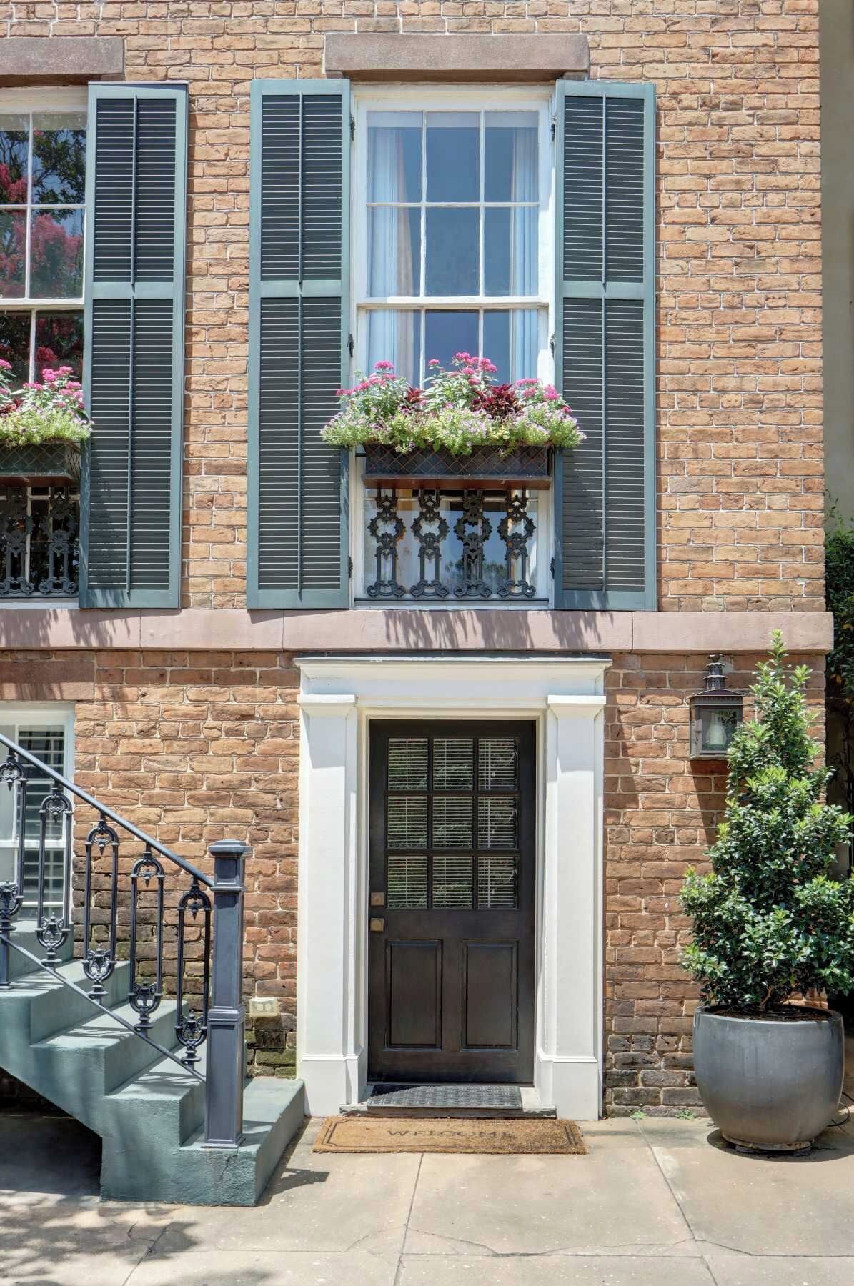A two-story building with a brick facade, a dark front door, and a small balcony with flower boxes.