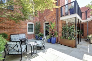 A brick building with a balcony, outdoor seating, and potted plants. - Brick & Beam | Luxury Garden Apartment | 1855 (Savannah)