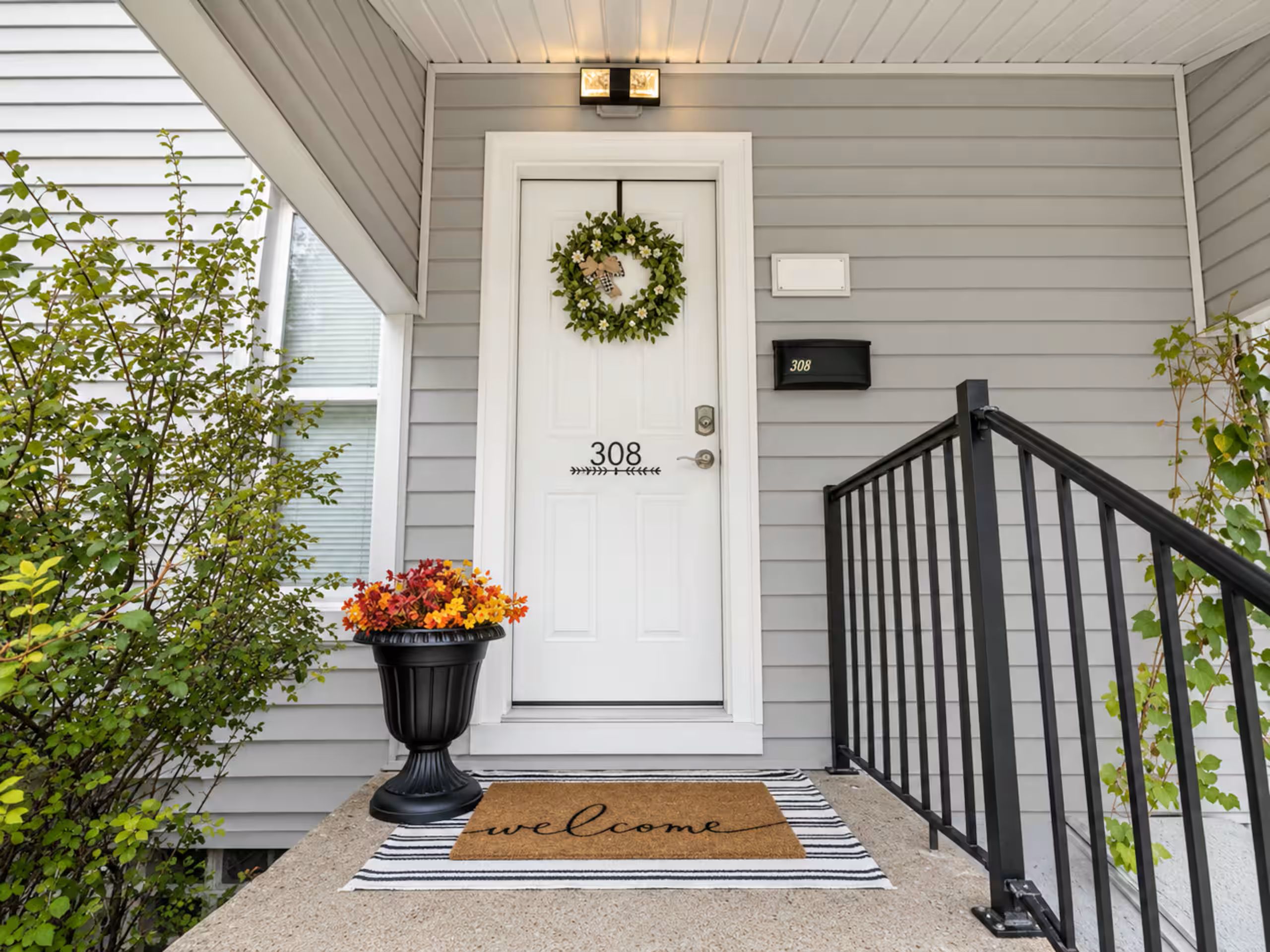 A front door with a number plate, a welcome mat, and a potted plant.