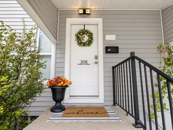 A front door with a number plate, a welcome mat, and a potted plant.