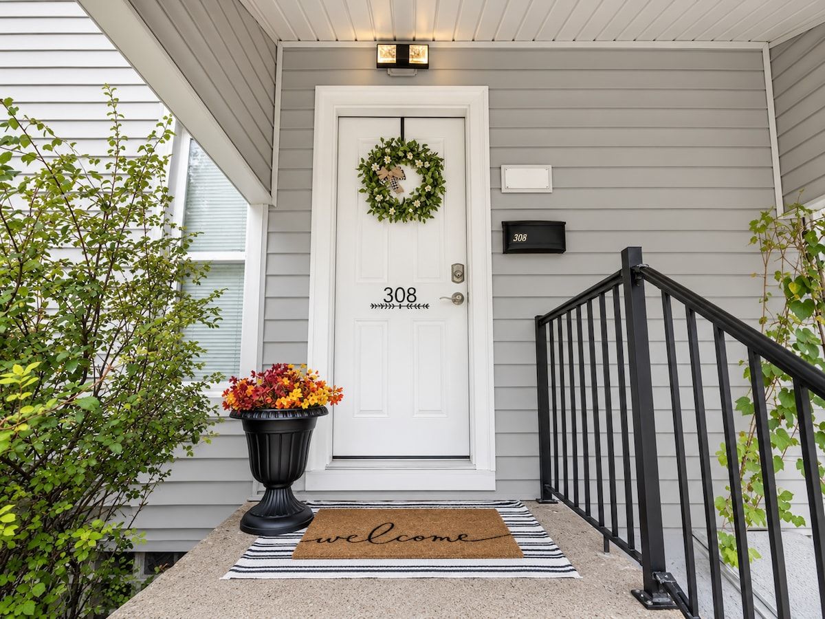A front porch with a white door, a mailbox, a black railing, and a welcome mat.