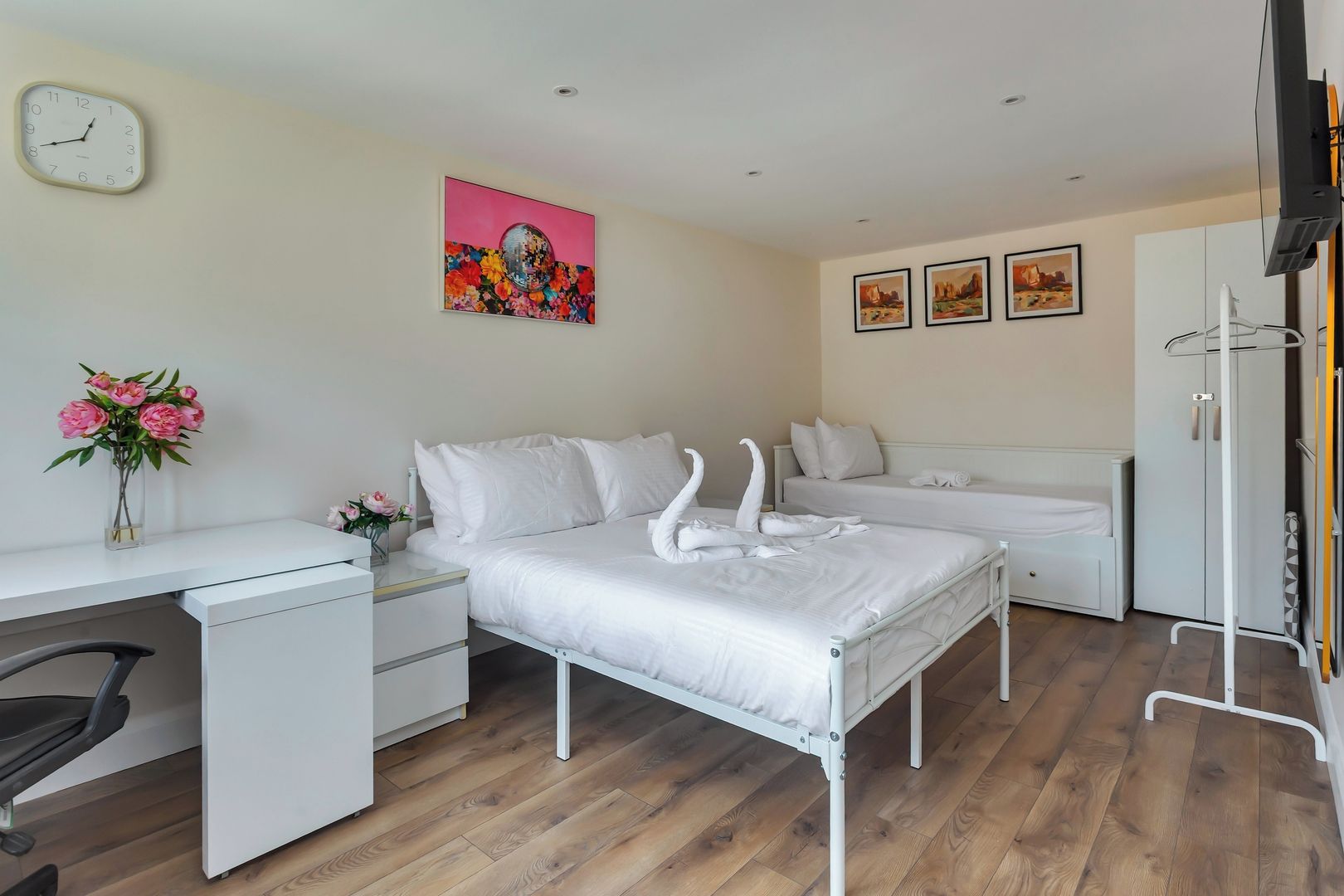 Un dormitorio moderno con cama, escritorio y silla. Hay un reloj en la pared y un cuadro sobre la cama.