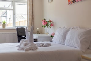 A hotel room with a bed, a desk, a chair, a window with a view of the outside, and a vase with flowers.
