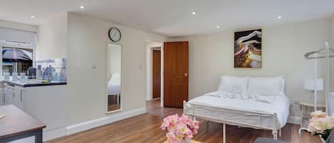 Une chambre d’hôtel moderne comprenant un lit, une petite table avec des fleurs, un canapé, un bureau et un coin cuisine.