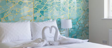 A neatly made bed with white linens and pillows, a bedside lamp, and a wall with a geometric pattern.