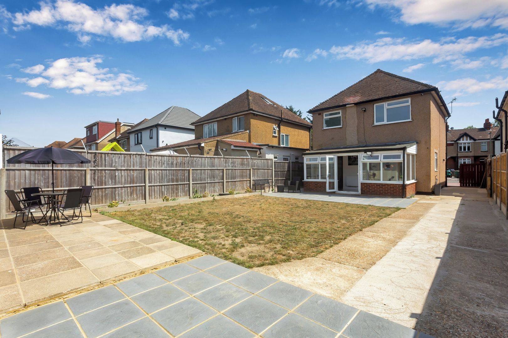 A residential backyard with a patio, a wooden fence, and a house with a tiled roof.