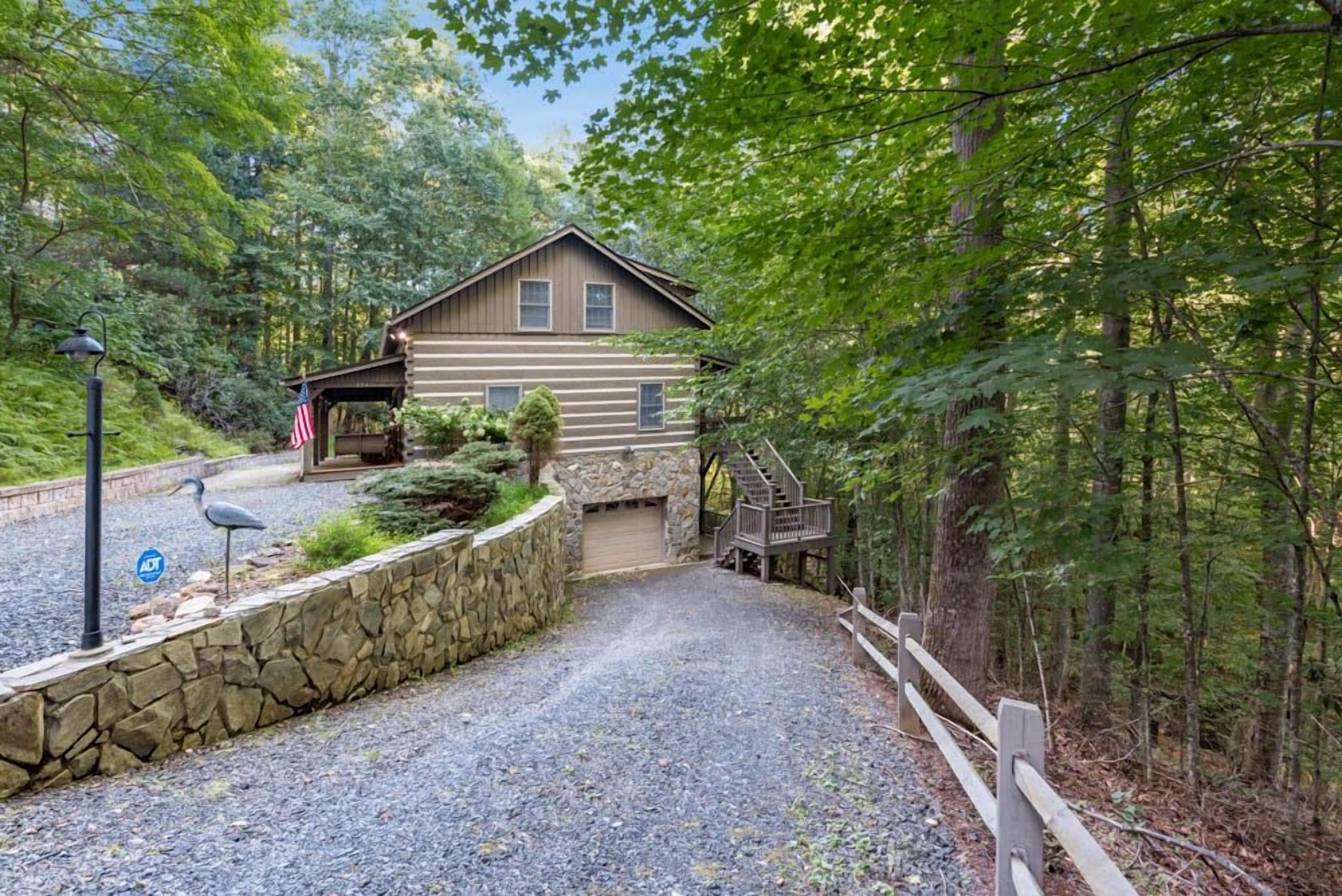 A cabin with a gravel driveway, a stone retaining wall, and a wooden staircase leading to the entrance.