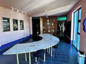 A conference room with a curved table, chairs, a bookshelf, and framed artwork on the walls. - Modern Sabana Retreat - Fast Wifi, Pool, Gym (San José)