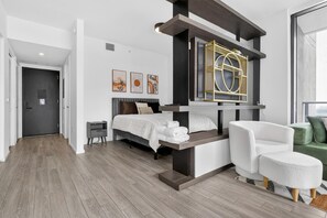 A modern bedroom with a bed, bedside tables, a seating area, and artwork on the wall. - Downtown Miami Studio with Balcony & Pool (Miami)