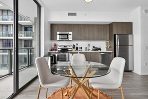 A modern kitchen with a glass dining table, white chairs, and stainless steel appliances. - Downtown Miami Studio with Balcony & Pool (Miami)