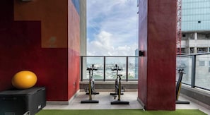 A gym with exercise equipment, a yoga ball, and a view of a cityscape through large windows. - Downtown Miami Studio with Balcony & Pool (Miami)