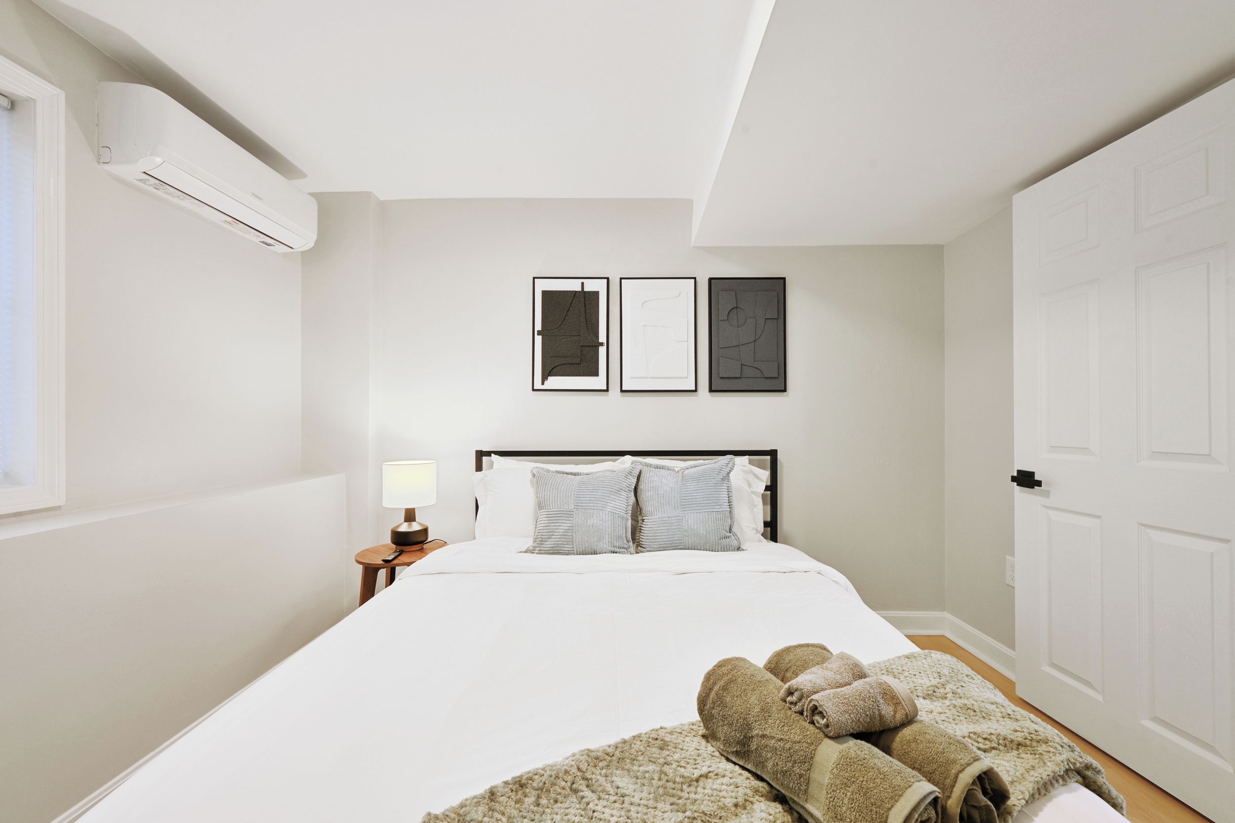 Une chambre d’hôtel avec un lit, une table de chevet avec une lampe et un climatiseur fixé au mur.