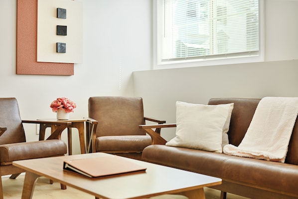 A modern living room with a brown leather sofa, a wooden coffee table, and a small side table with a vase of flowers.