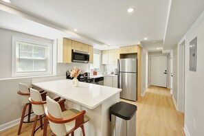 Une cuisine moderne dotée d’un îlot central, de meubles en bois, d’appareils électroménagers en acier inoxydable et d’un coin repas avec des chaises.