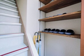 Een trap met witte treden en een rode accentkleur, die leidt naar een plateau met houten planken waarop schoenen en paraplu's staan.