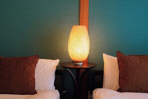 Een kamer met twee bedden, een ronde tafel met een lamp en een gestructureerde muur.