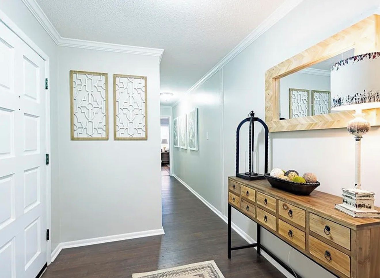 A hallway with a wooden dresser, a mirror, and framed artwork on the walls.