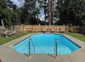 A rectangular swimming pool with metal ladders, surrounded by a wooden fence, grass, and trees. - 3-bedroom house in delightful Valdosta with pool, jacuzzi, and cool AC. (Valdosta)