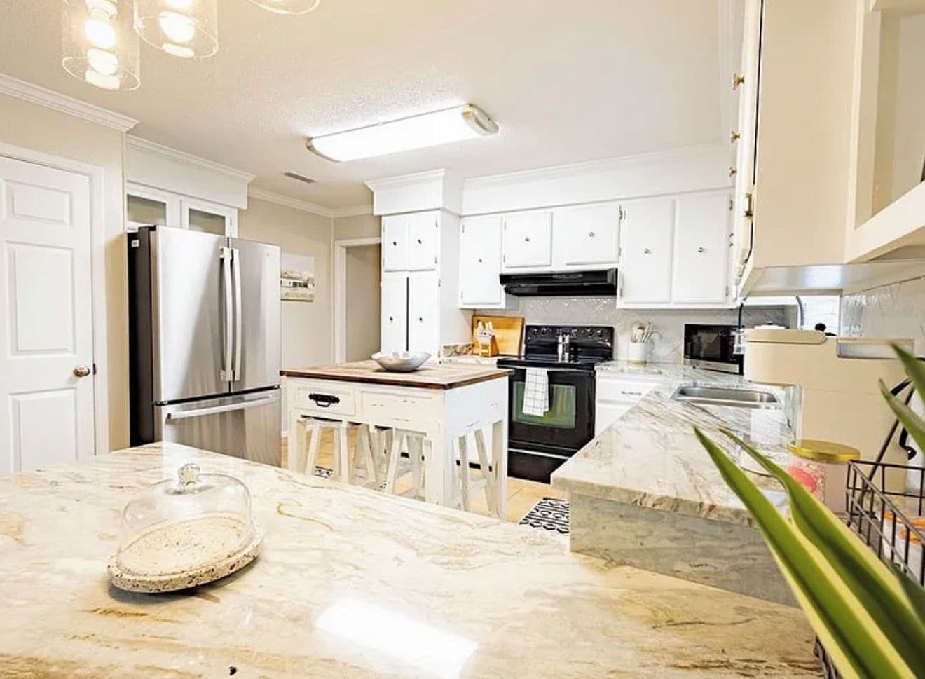 A modern kitchen with white cabinetry, stainless steel appliances, and a marble countertop.