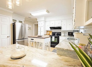A modern kitchen with white cabinetry, stainless steel appliances, and a marble countertop. - 3-bedroom house in delightful Valdosta with pool, jacuzzi, and cool AC. (Valdosta)