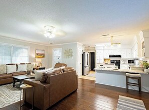 A modern living room with a brown sofa, a coffee table, and a dining area with a kitchen island. - 3-bedroom house in delightful Valdosta with pool, jacuzzi, and cool AC. (Valdosta)